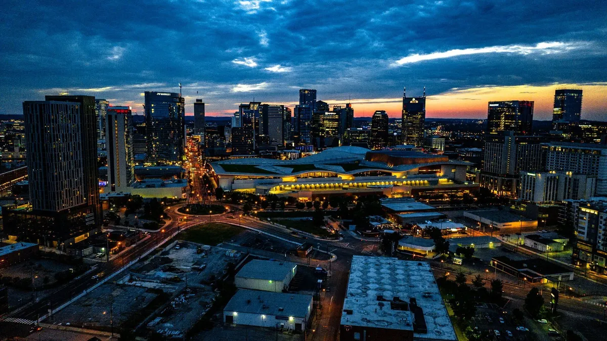 A panoramic view of the city skyline at dusk, with glowing street lights, distant mountains, and dynamic cloud formations. The urban landscape exudes energy and adventure, inviting guests to explore Nashville’s vibrant attractions.