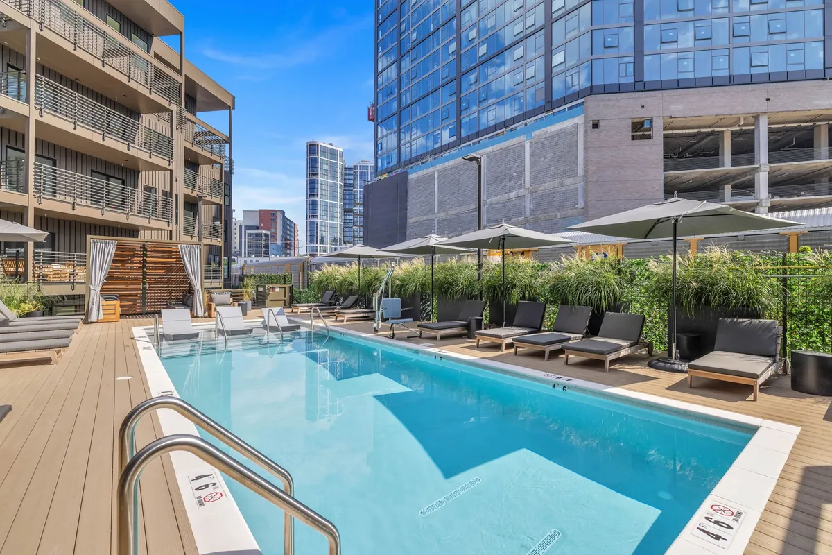 A vibrant outdoor swimming pool area featuring inviting lounge chairs, lush surrounding greenery, and the facade of the building. The space is designed for relaxation and social gatherings, evoking a sense of summer leisure and community.