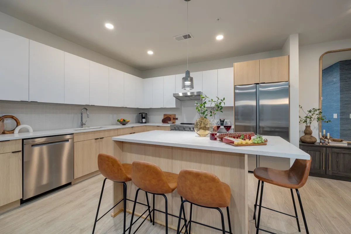 The image showcases a kitchen island with seating, modern stainless steel appliances, and a table set for a dinner party, with fresh greenery adding a lively touch. The space feels warm, functional, and ready for both cooking and entertaining.
