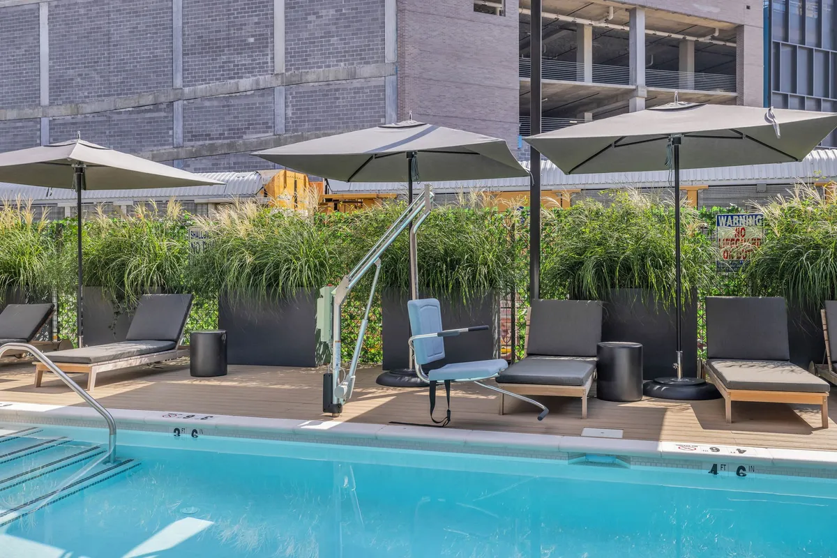 A sparkling outdoor swimming pool is framed by sun loungers, umbrellas, and landscaped greenery, inviting guests to unwind and socialize. The setting is bright and serene, perfect for relaxing after a day of city exploration.