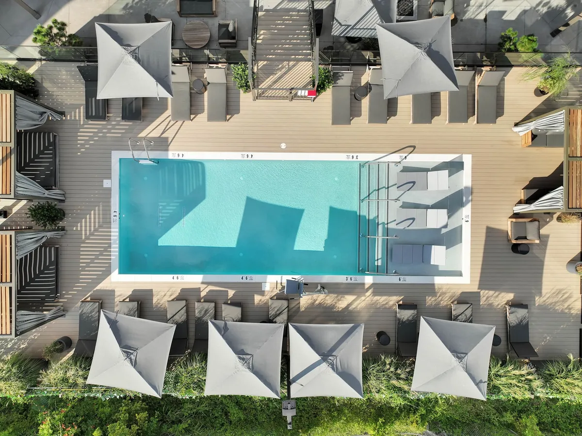 A sparkling swimming pool surrounded by sun loungers and shade umbrellas, with a spacious decking area inviting guests to swim, sunbathe, or socialize. The tranquil, resort-like setting is perfect for both relaxation and lively gatherings.