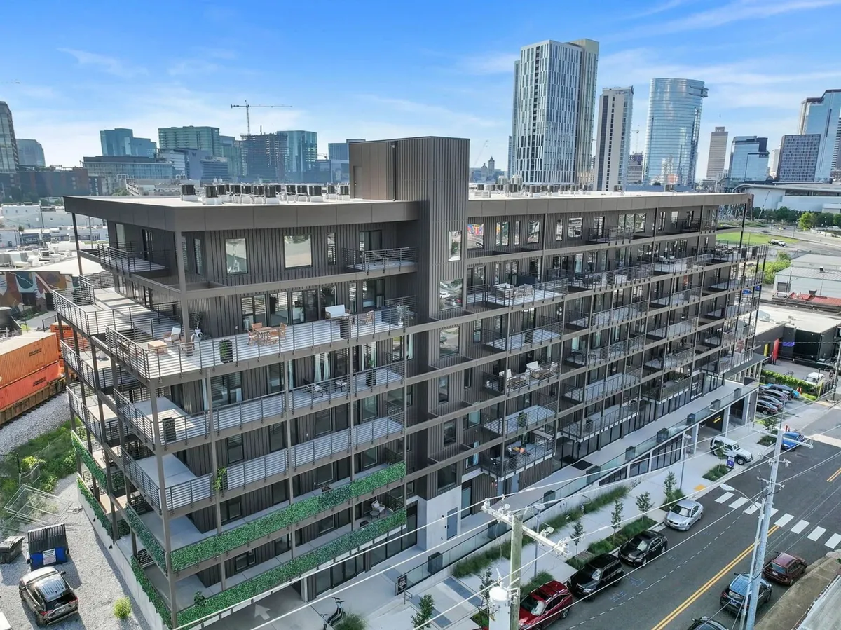 A modern urban building with lush balconies, set against a vibrant city skyline. The architecture suggests upscale living, with visible balconies hinting at dynamic communal spaces and a connection to the energetic downtown environment.