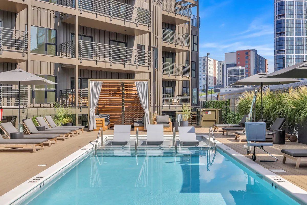 The exterior pool area features sleek lounge chairs, a sparkling swimming pool, and the building’s modern facade in the background. The space is ideal for unwinding after a workday, networking, or socializing in a high-end outdoor environment.