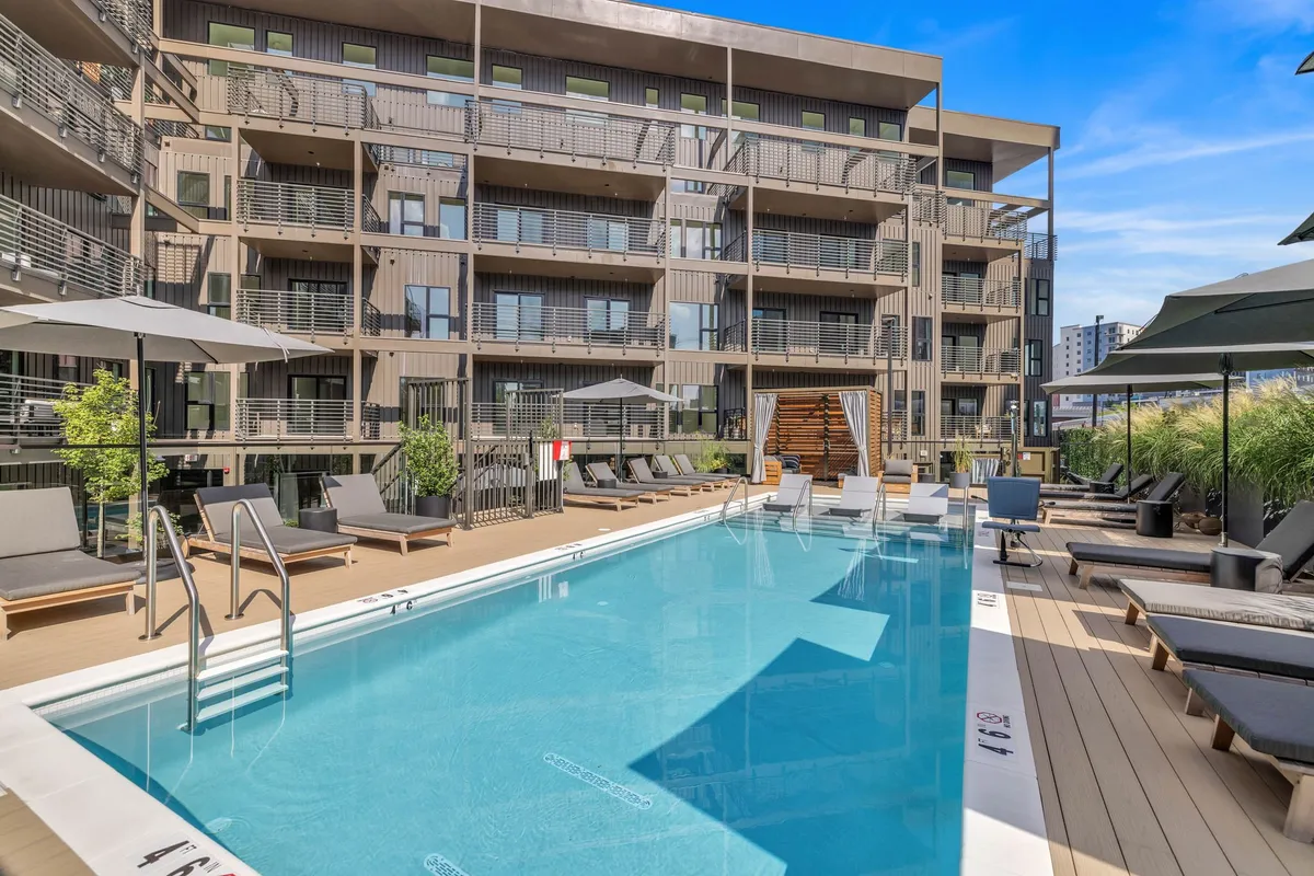An inviting outdoor swimming pool with lounge chairs, balconies, and lush landscaping. The amenities evoke relaxation and socializing after an active day in the city.