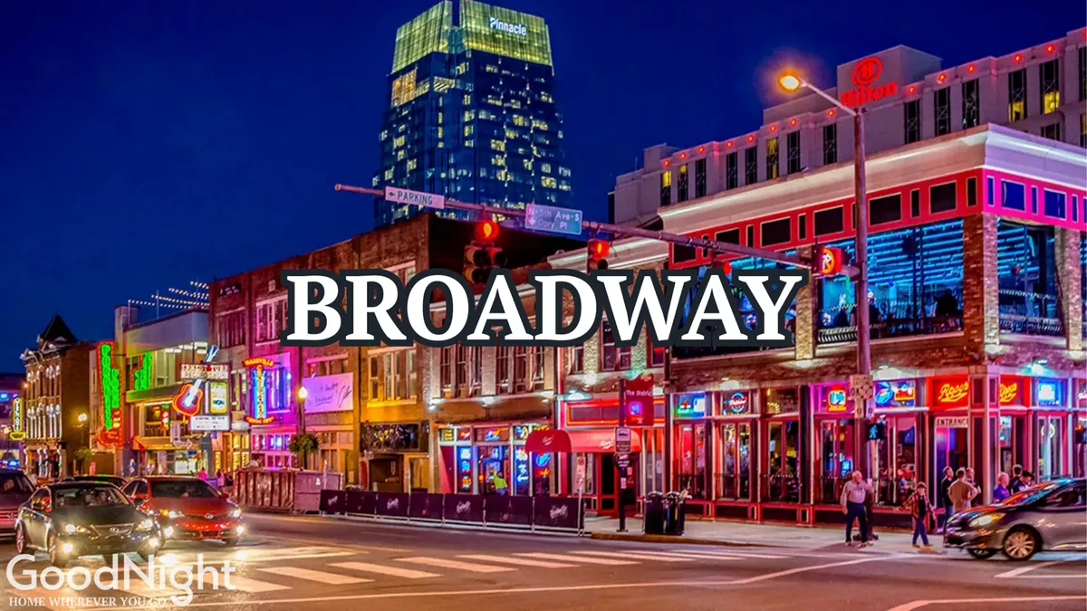 A bustling nighttime street scene lined with neon signs, lively storefronts, and groups of people strolling, eating, and enjoying the city energy. The image evokes Nashville's famed honky-tonks, entertainment, and nightlife.